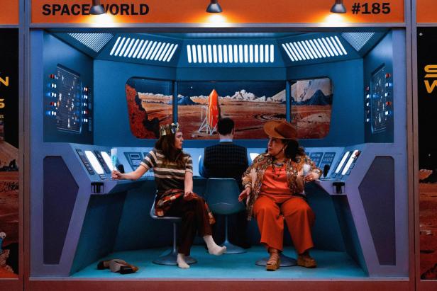 Two women with champagne glasses sit in a spaceship setting