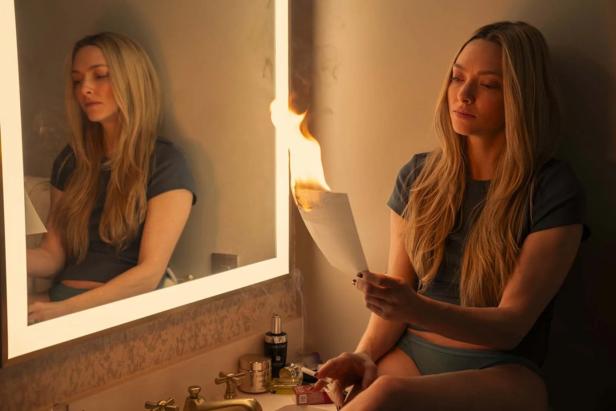 Amanda Seyfried sits in front of a mirror and holds burning paper in her hand