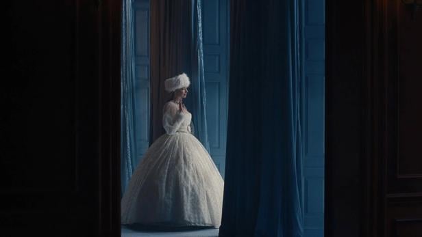 Margot Robbie in a white dress between dark curtains