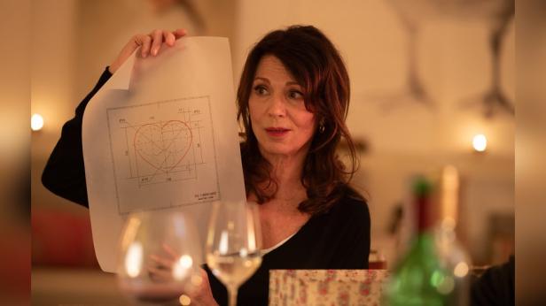 In her film role, Iris Berben holds up a piece of paper at a dining table on which a heart has been drawn