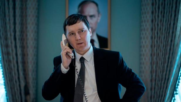 Paul Dano in film role on the phone - in the background there is a picture of Jude Law as Putin