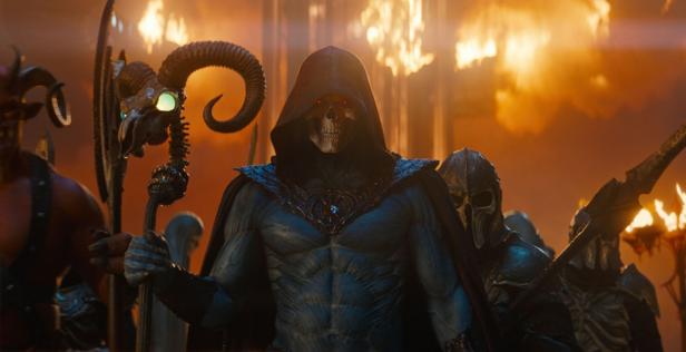 Skeletor with skull mask and staff stands before an army in a fiery, dark environment.