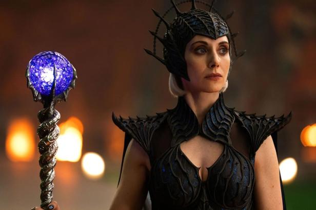Woman in black spiky armor with helmet holds a staff with glowing blue ball.