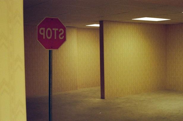 An upside down stop sign stands in an empty, yellow-lit room with carpeted floors and partitions.
