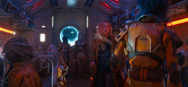 A blonde woman stands in a futuristic spaceship interior among various alien creatures.