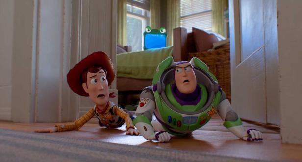 Woody and Buzz crawl frightened through a hallway while a tablet with eyes sits on a bed in the background.