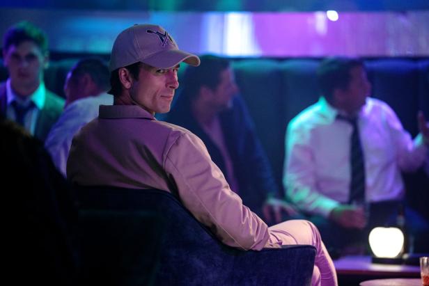 Glen Powell sits in the club in a film role