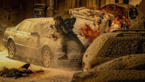 Man jumping between cars in a snowy street scene from explosions.