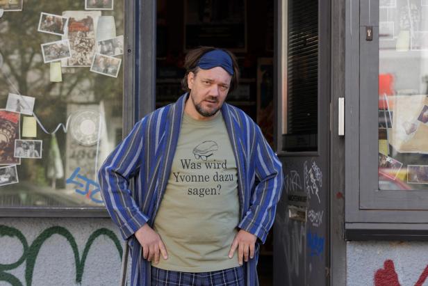 Charly Hübner stands in a film role in an open door of a shop