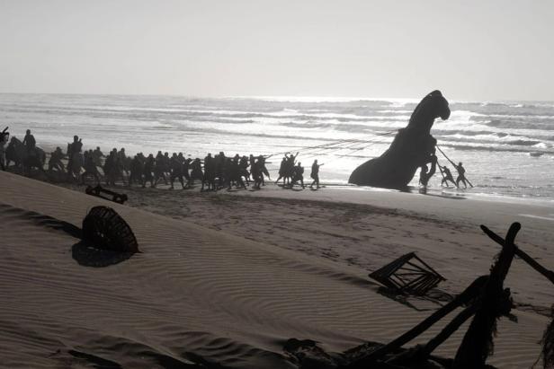 People pull the giant Trojan horse away from an ocean beach.
